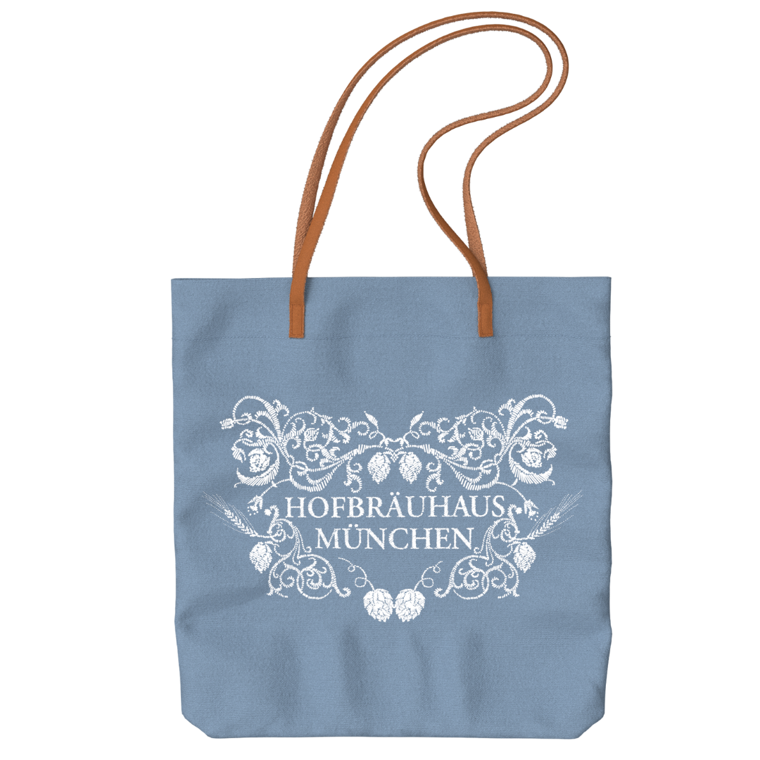  „Hellblaue Tragetasche mit braunen Ledertrageriemen und mit floraler Verzierung und HB-Logo in weiß auf der Vorderseite.“