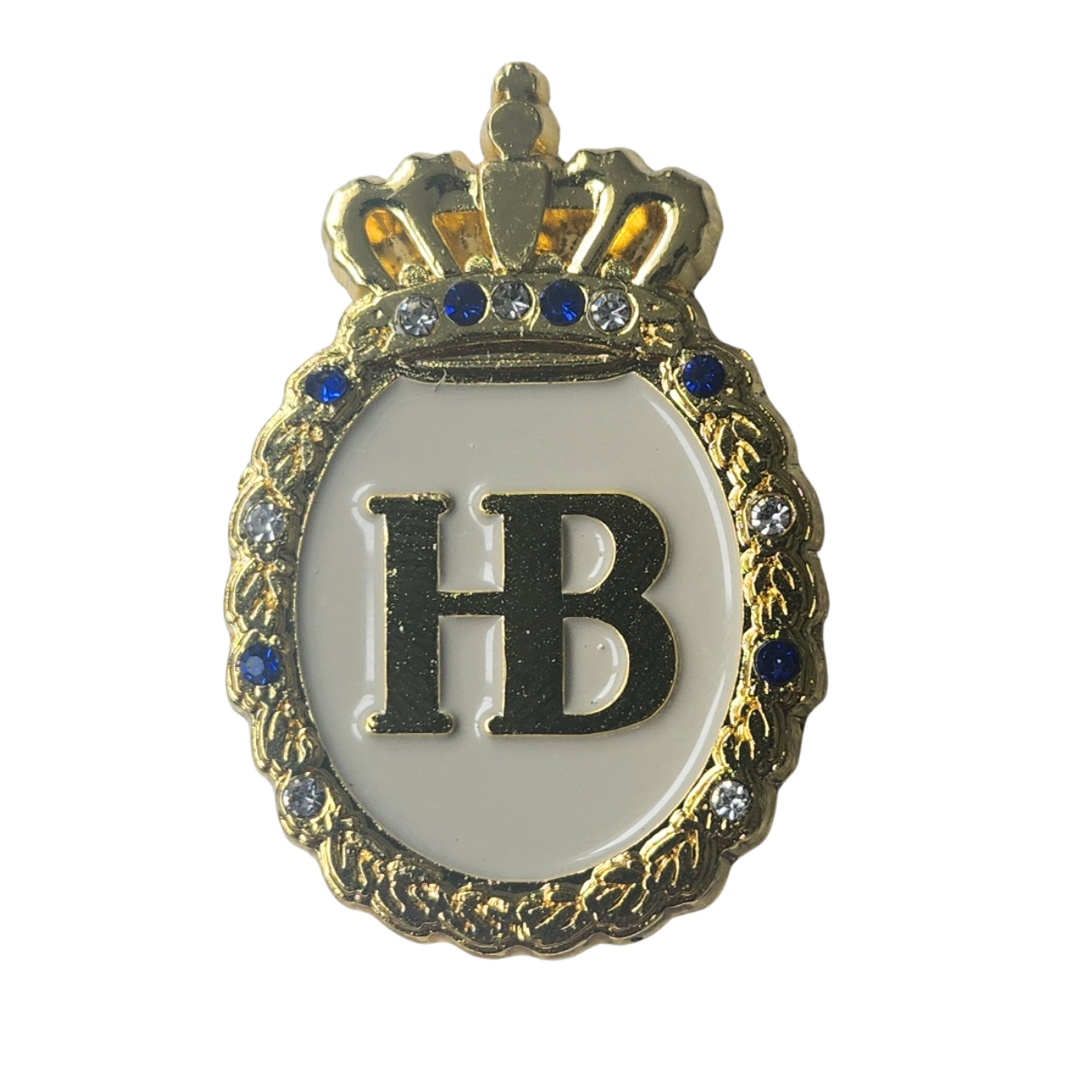 „Eleganter Ansteckpin mit weißem Hintergrund und zentralem Schriftzug ‚HB‘. Über den Buchstaben befindet sich eine goldene Krone. Der Pin ist von einem goldfarbenen, kunstvoll verzierten Rahmen umgeben, in den mehrere blaue Schmucksteine eingelassen sind.