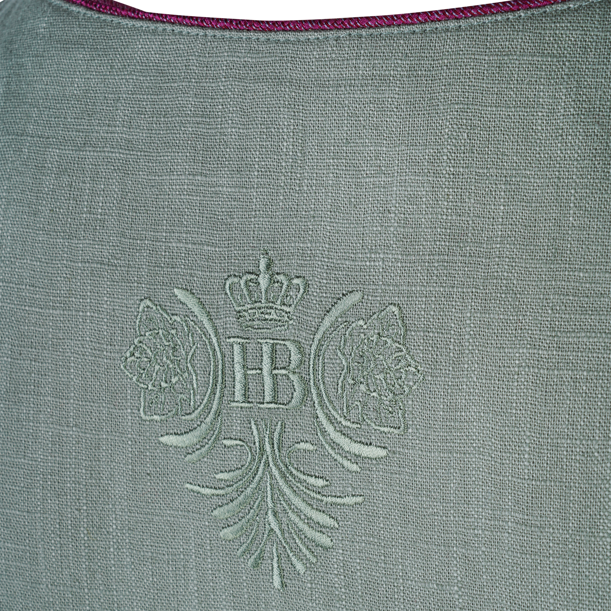 Nahaufnahme der Rückseite eines grünen Dirndl-Mieders mit eingewebtem HB-Logo, Krone und floralen Ornamenten in derselben Stofffarbe.