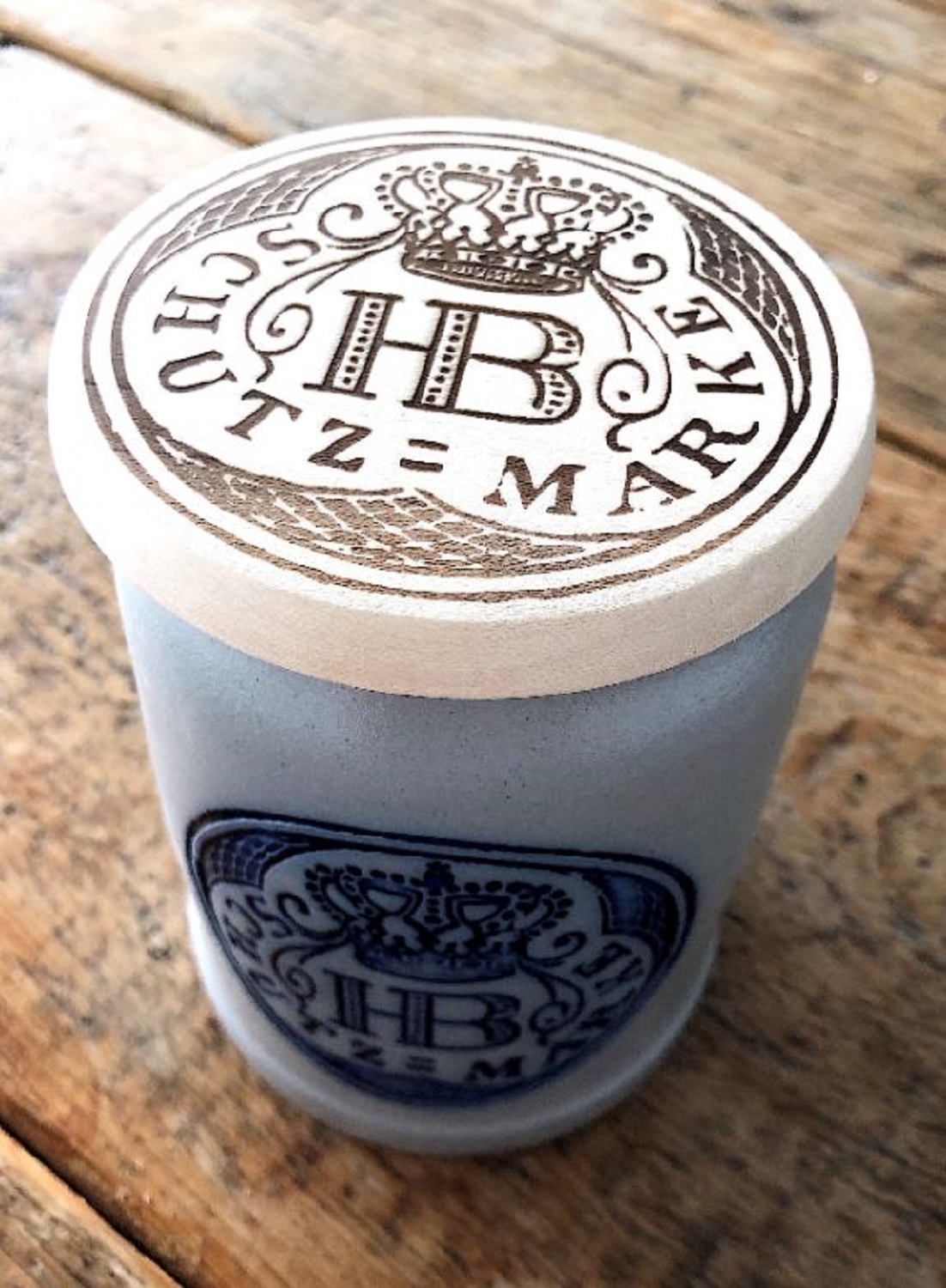 Holz-Bierdeckel mit eingraviertem HB-Logo und der Aufschrift 'Schutzmarke' auf einem Steinkrug platziert.