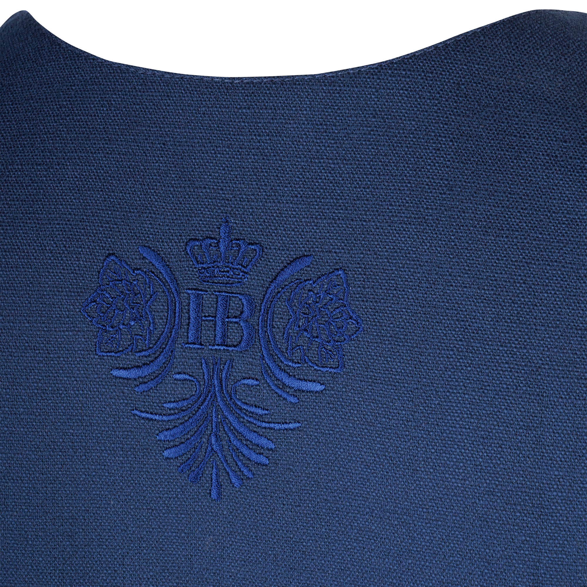 Nahaufnahme des Rückenteils eines dunkelblauen Dirndls mit einem eingewebten Emblem: zentral das "HB"-Logo mit Krone, flankiert von zwei Hopfendolden und floralen Ornamenten.