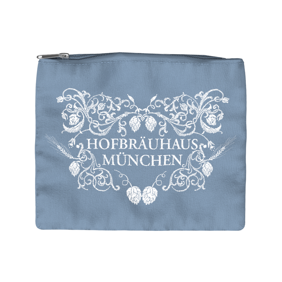 „Rechteckige Kosmetiktasche aus hellblauem Stoff mit silberfarbenem Reißverschluss an der Oberseite. Auf der Vorderseite befindet sich ein weißer Aufdruck mit floralen Mustern und dem Schriftzug ‚HOFBRÄUHAUS MÜNCHEN‘.“